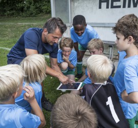 Coach with tablet and young football players on football ground